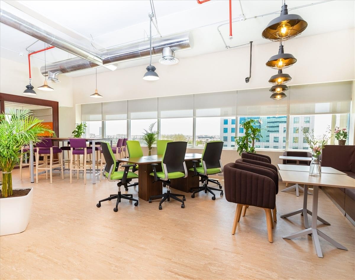 Large communal breakout space featuring greenery, pendant lighting, and comfortable seating.