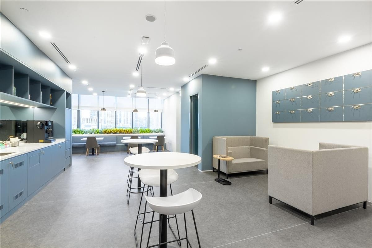 Bright communal break area with blue cabinetry, cafe seating, and modern pendant lighting.