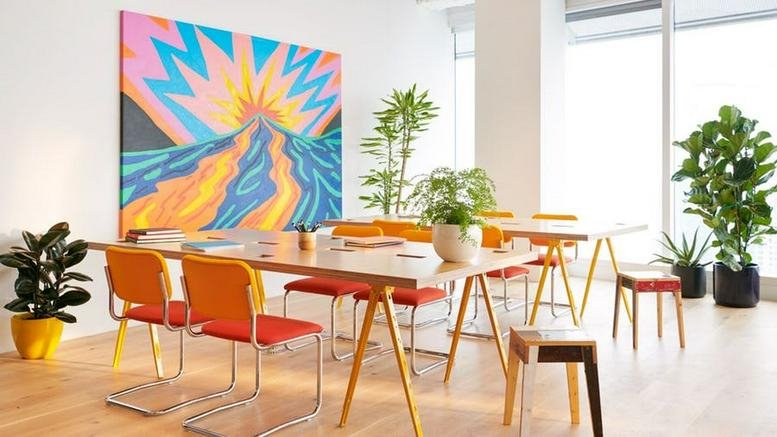 Brightly lit meeting area at Hub 71, Al Khatem Tower, featuring a colorful mural and wooden tables with orange chairs.