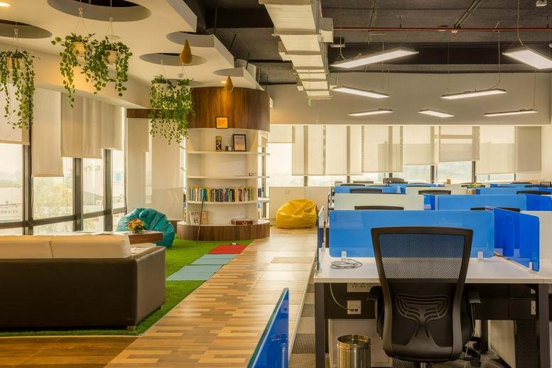 Open-plan workspace at Indiqube IT Kode, Echelon, Pashan Link Road featuring blue desks and hanging plants.