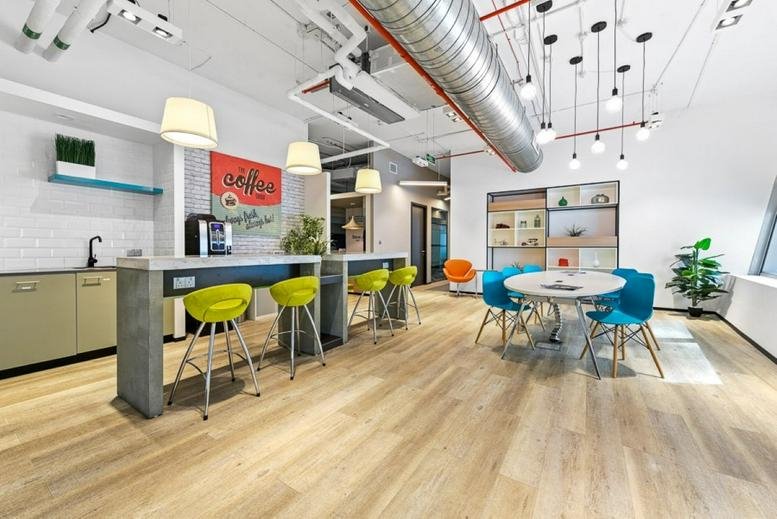 Open-plan common area at Iris Bay Tower with colorful seating, high-top tables, and exposed ceiling ducts.