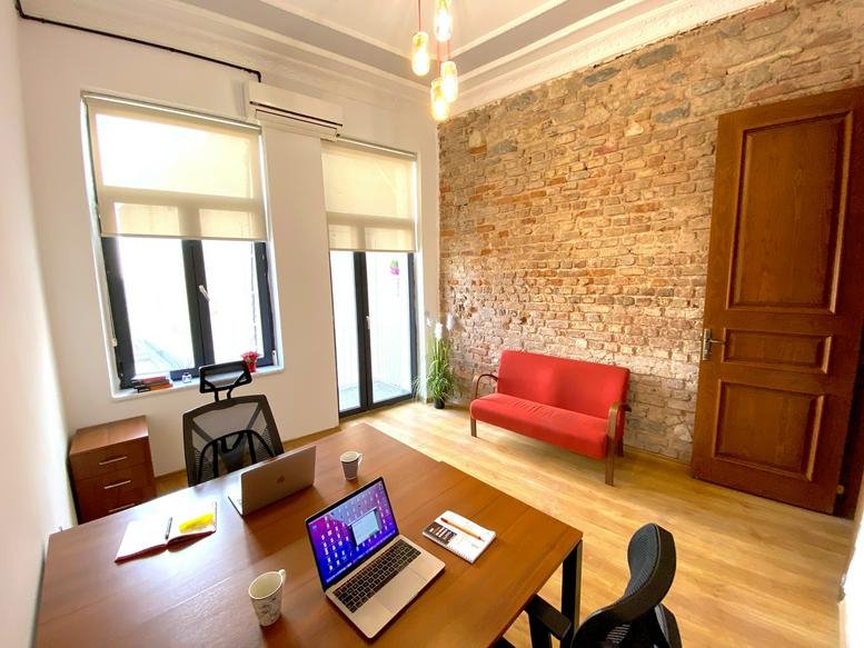 Spacious office room with a red sofa, exposed brick wall, and natural light.
