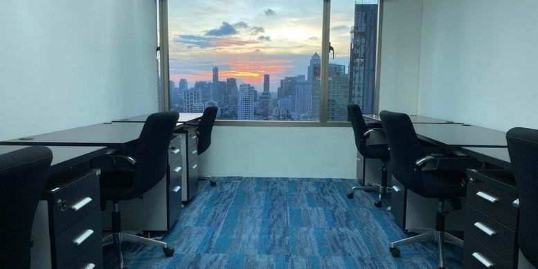 Modern workspace at the Jasmine City Building featuring desks facing a sunset city skyline view.
