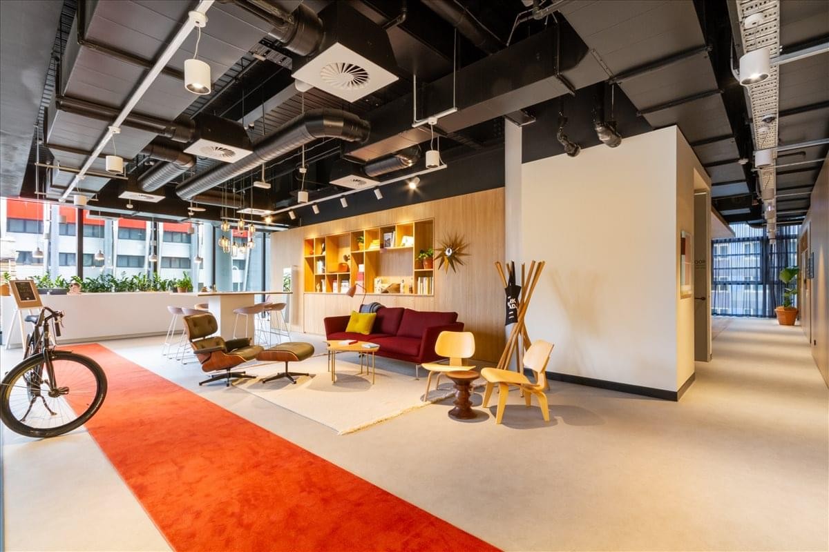 Spacious lounge area with a red sofa, designer chairs, and exposed ceiling ductwork.