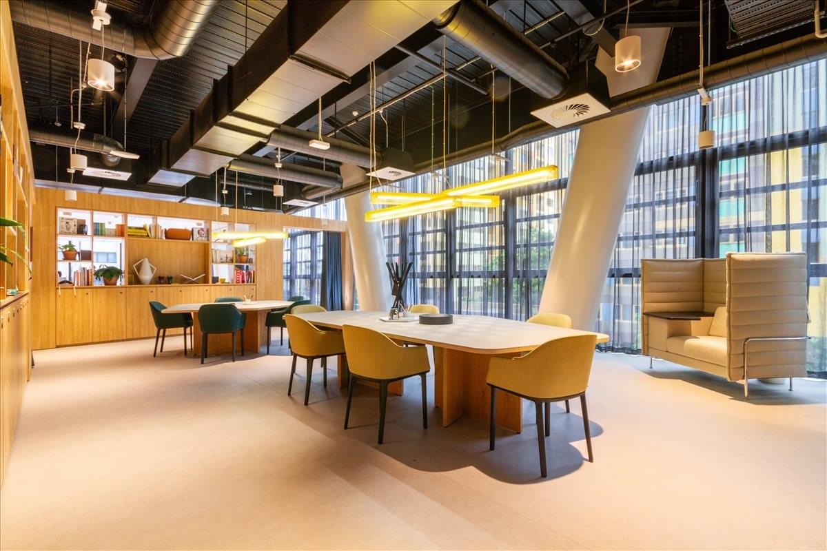 Expansive coworking area with yellow dining chairs, long tables, and industrial ceiling details.