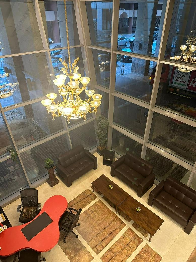 Double-height lobby lounge featuring brown leather sofas, a large chandelier, and a unique red desk.