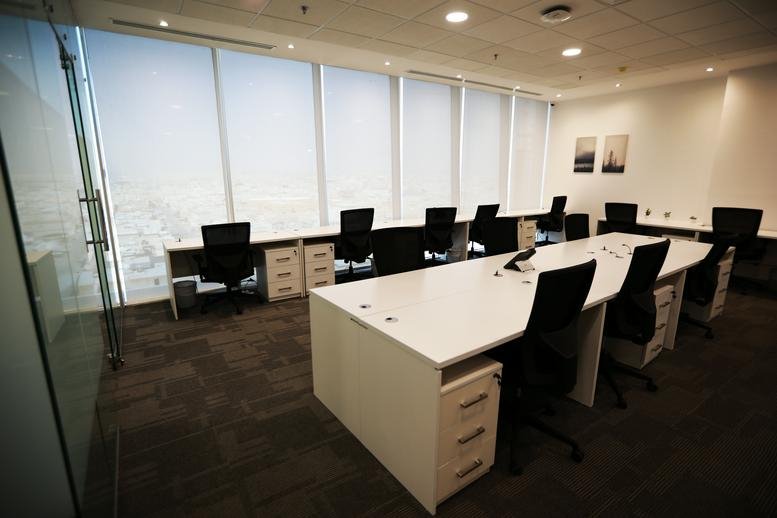 Bright open-plan workspace with rows of white desks and ergonomic black chairs.