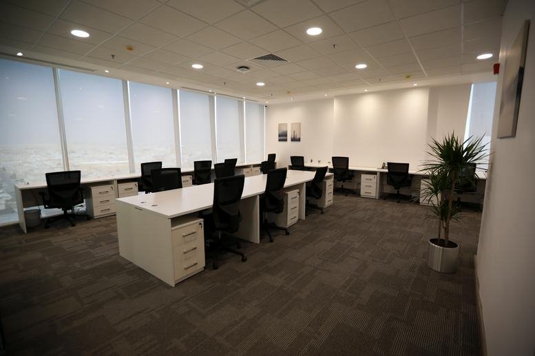Bright coworking area with white workstations, potted greenery, and abundant natural light.