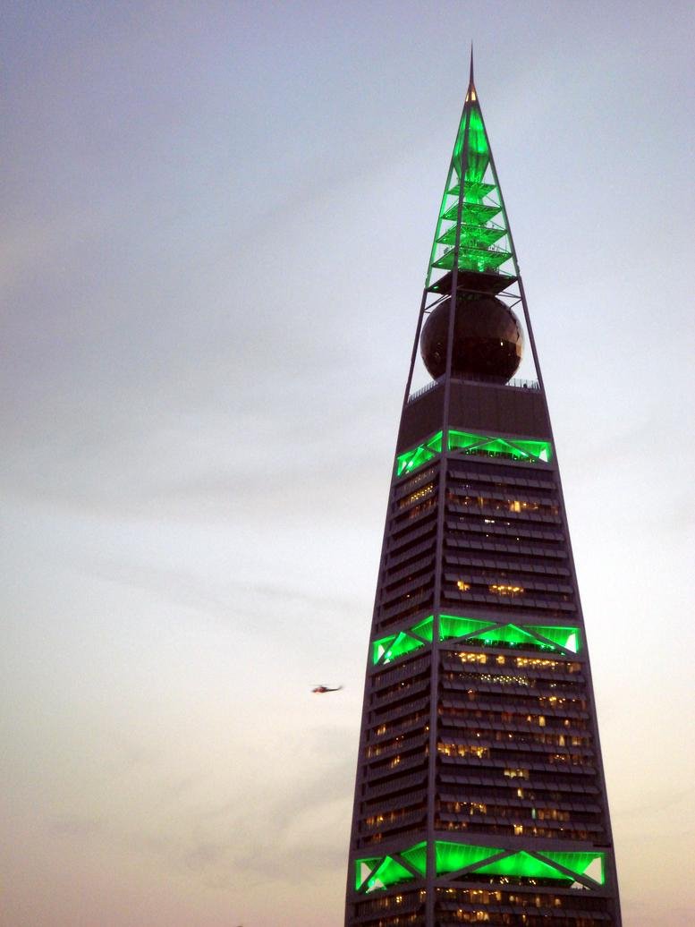 Exterior view of the Al Faisaliah Tower on King Fahd Road with distinctive green lighting and golden sphere.