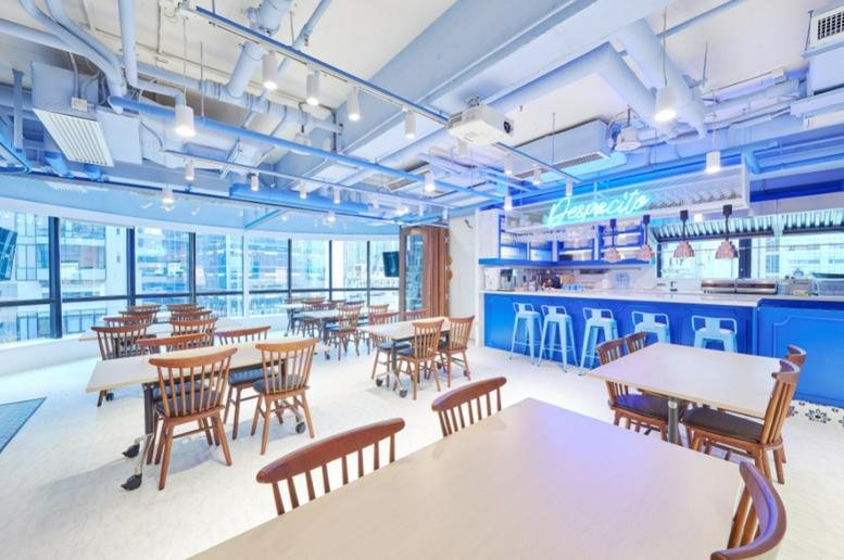 Spacious communal cafe at Silver Fortune Plaza with blue accents, wooden dining sets, and exposed ceiling pipes.