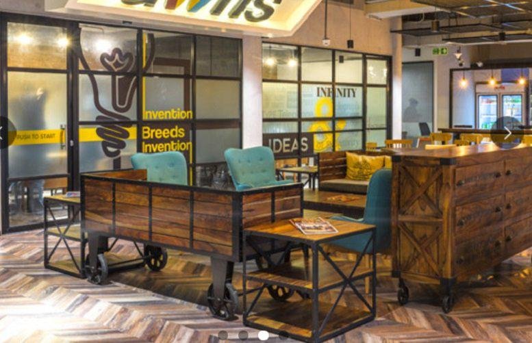 Vibrant communal lounge at G. K. Mall (L3 & L4) with rustic wooden furniture and teal accent chairs.