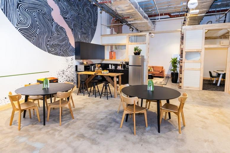 Communal break area with round dining tables and a feature wall mural at Macarthur Square, 200 Gilchrist Drive.