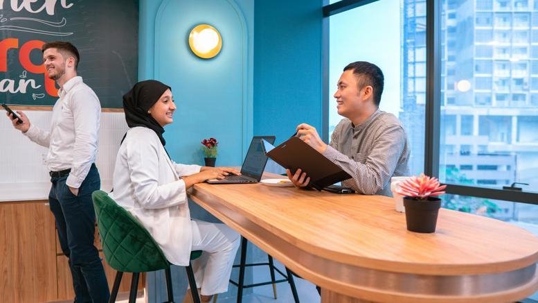 Spacious coworking space at Menara UOA Bangsar with people working at a long wooden table.