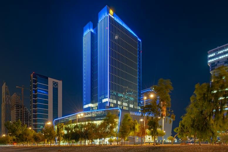 Evening exterior view of the modern glass-facade Burj Alfardan building with blue accent lighting.