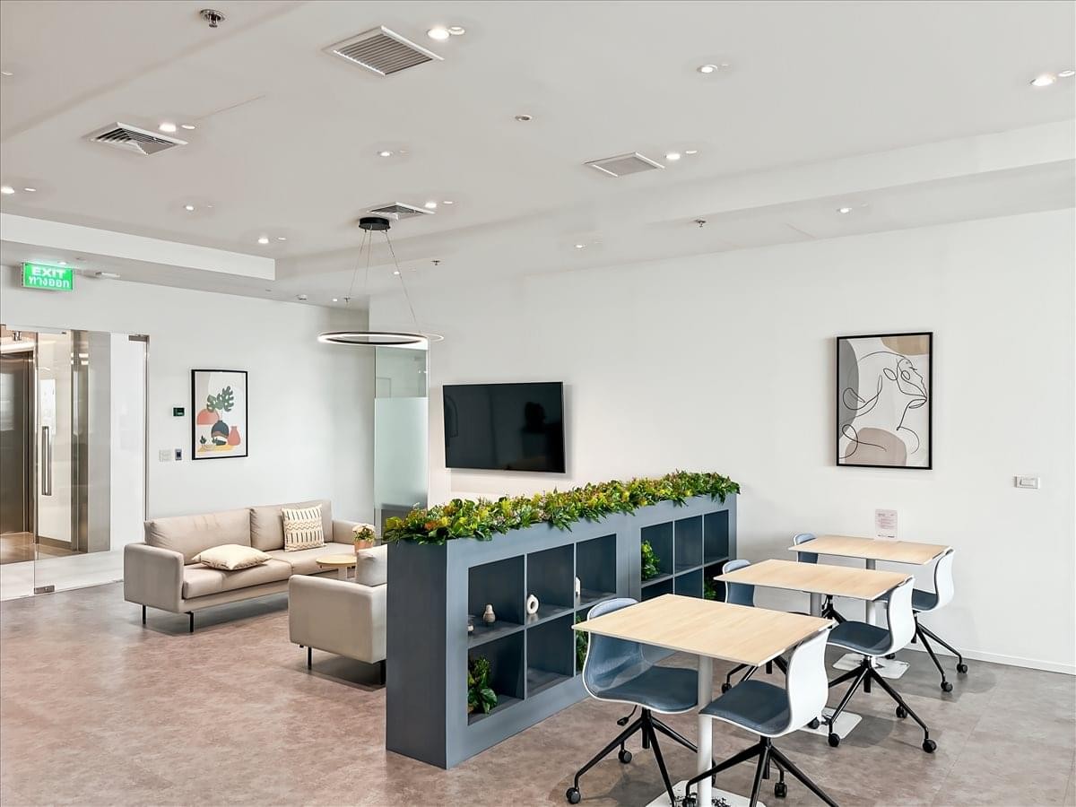 Spacious communal lounge at WHA Tower featuring modern furniture, a media screen, and planters.