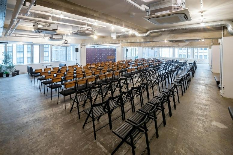Large meeting room at Nagatacho GRiD 2-5-3 Hirakawa-cho, Tokyo with rows of wooden chairs and industrial ceilings.