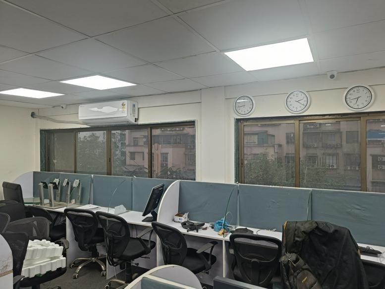 Open-plan workspace at NBC Complex with rows of desks, office chairs, and wall-mounted clocks.