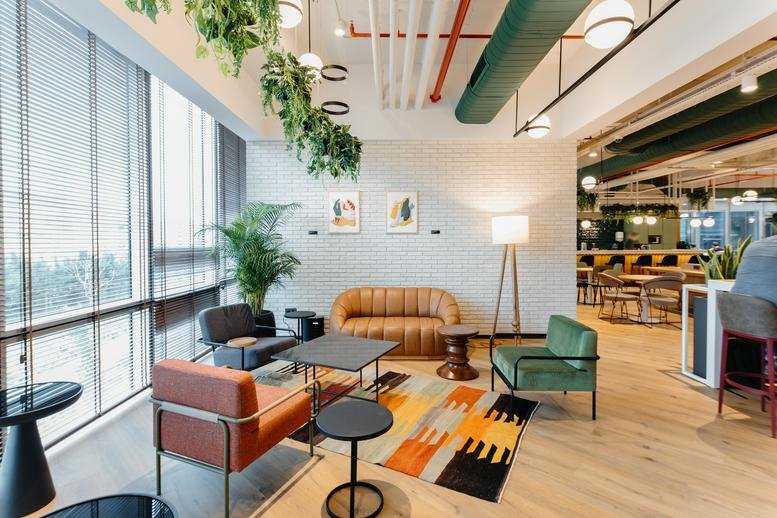 A bright, modern lounge at Nida Kule Ataşehir featuring plants, a tufted leather sofa, and colorful rug.
