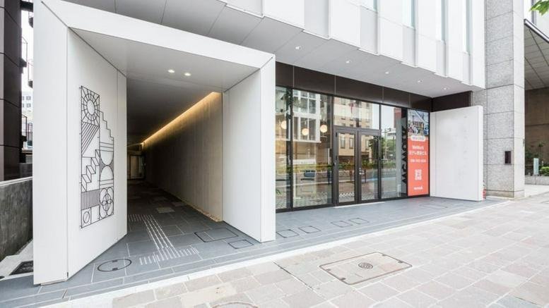 Ground level entrance to the Nippon TV Yotsuya Building featuring a modern white geometric portal and glass doors.