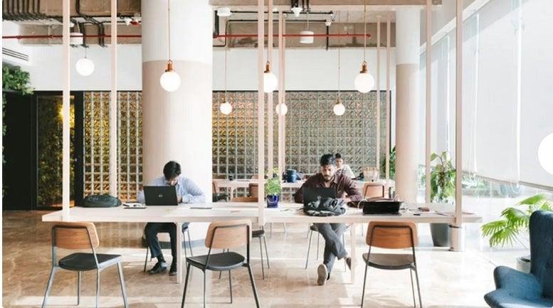 Spacious communal coworking area with long white tables, pendant lighting, and natural light at Marol Industrial Area.