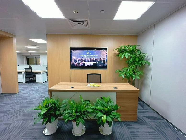 Wooden reception desk with green potted plants and a large digital screen on the wall.