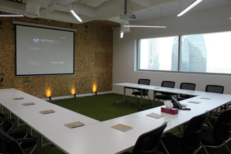 Spacious u-shaped training room at 48 Burj Gate featuring a green carpet and projector screen.