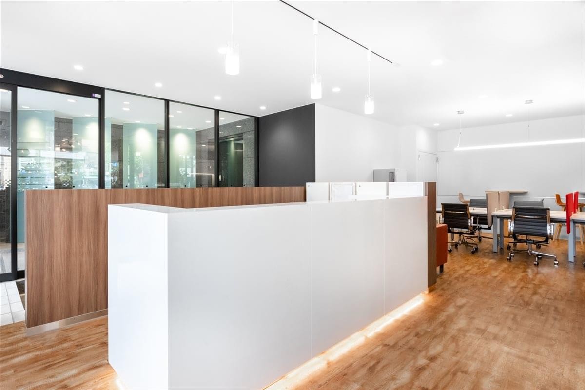 Sleek reception area with a white front desk, warm wood flooring, and pendant lighting.