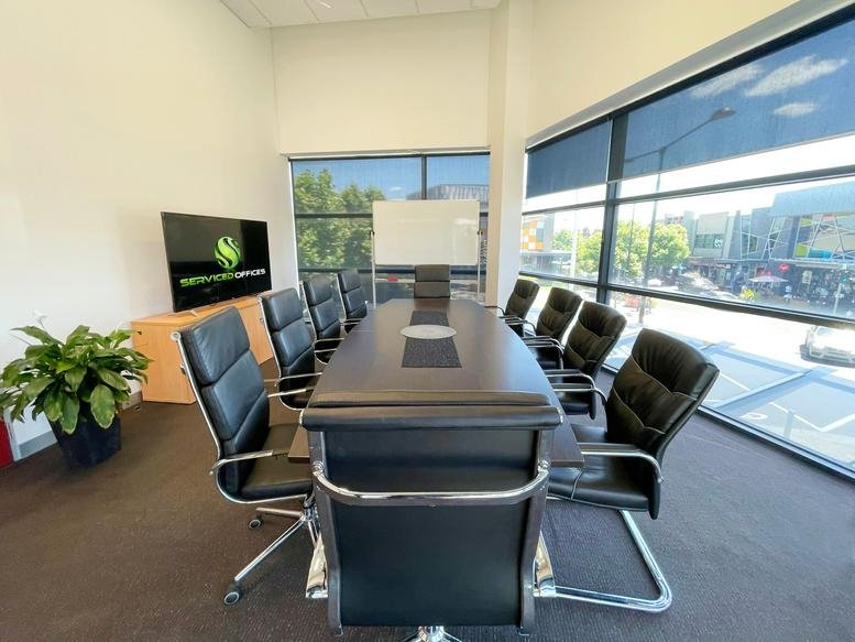 Spacious boardroom with a long black table, leather chairs, and large windows with street views.
