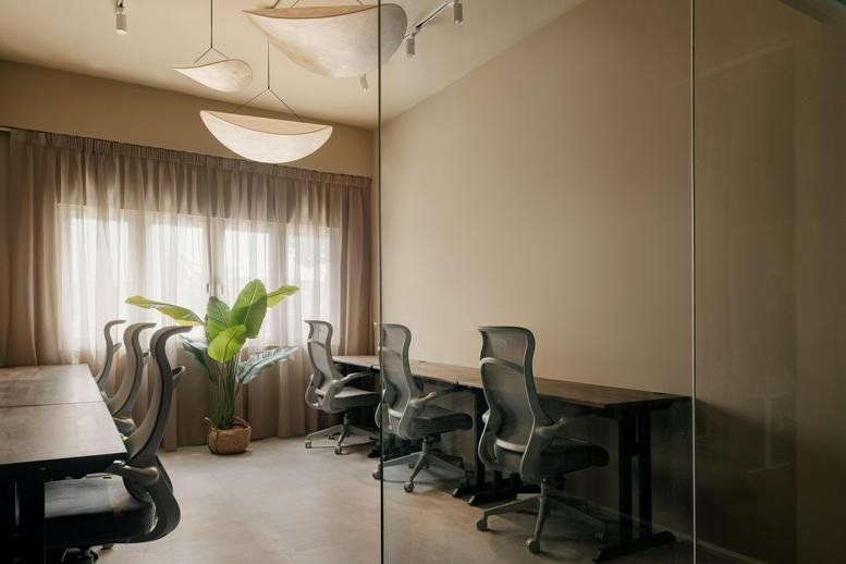 Meeting room seen through a glass partition with a long table, grey chairs, and a potted plant.