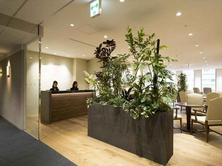 Spacious reception area of the Saiwai Building with a modern wooden desk and large planter with lush greenery.