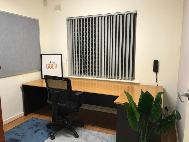 Spacious corner office at 1 Clark Terrace with a large desk, mesh chair, and a potted plant.