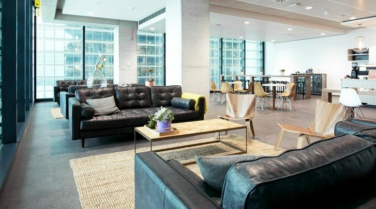 Spacious communal lounge with black leather sofas, wooden coffee tables, and floor-to-ceiling windows.