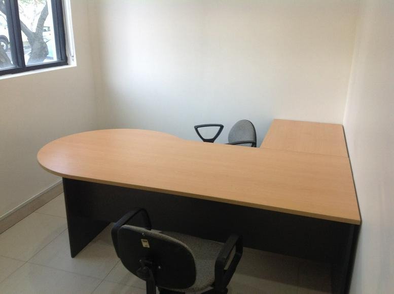 Spacious L-shaped wooden desk in a private office with grey ergonomic chairs.