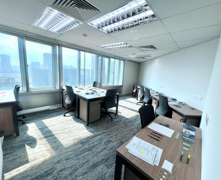 Spacious open-plan office with multiple rows of workstations and floor-to-ceiling windows.