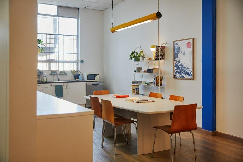 Bright communal kitchen and dining area with a long white table and yellow pendant light.