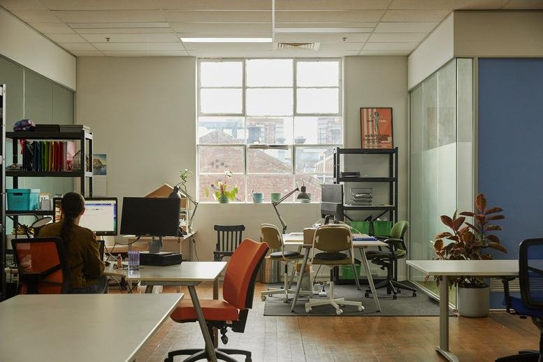 Open-plan workspace at MillHaus, 112 Argyle Street, Fitzroy, featuring modern desks and orange chairs.