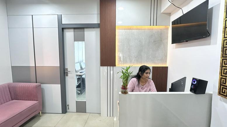 Reception area at 115 Poonamallee High Road featuring a white front desk, pink sofa, and wall-mounted TV.