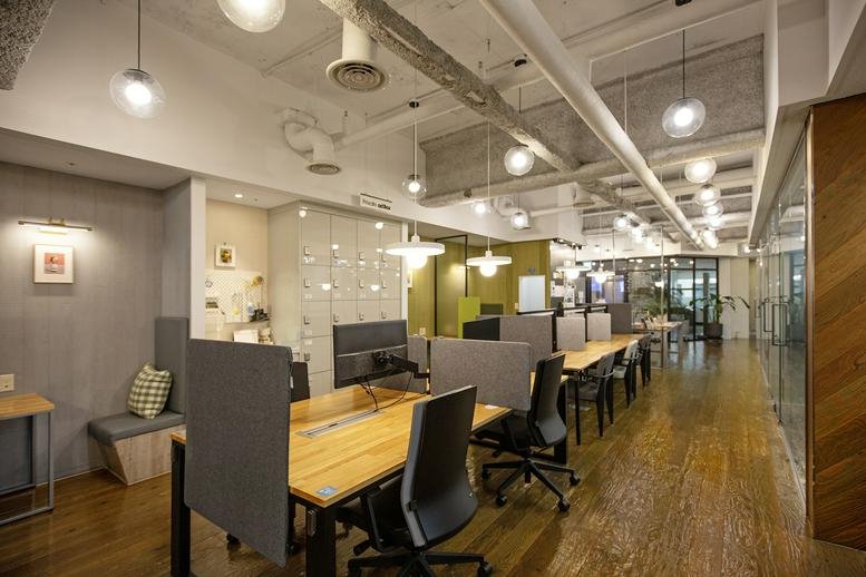 Coworking space featuring long wooden tables, industrial lighting, and glass partitions.