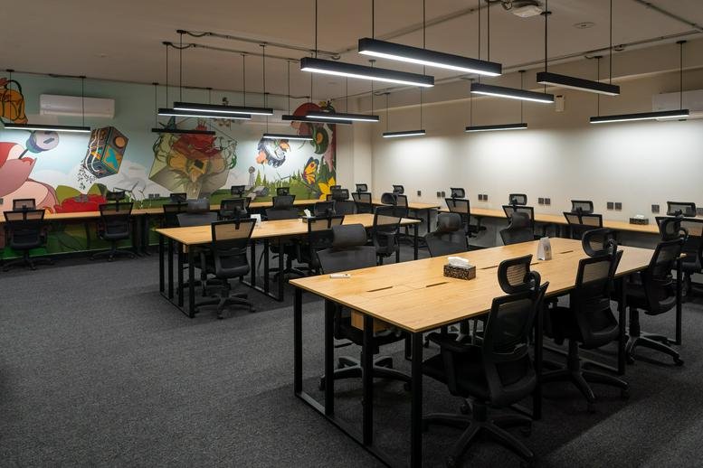 Spacious open-plan workspace with multiple wooden desks, black chairs, and a colorful wall mural.