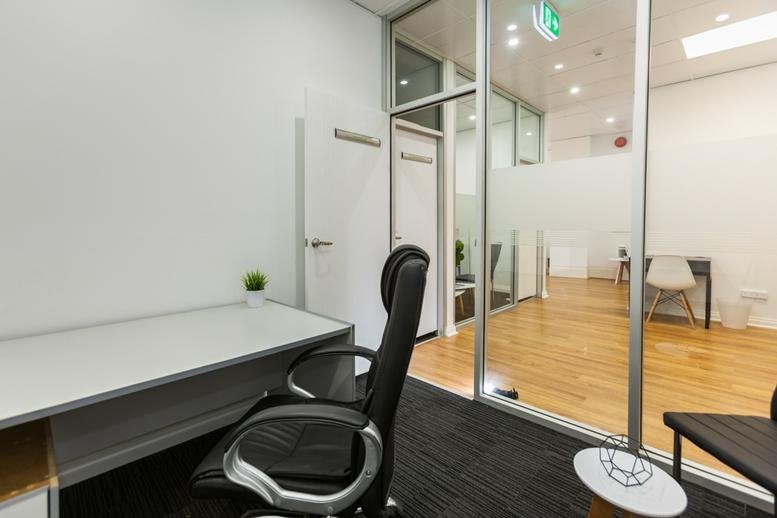Bright workspace with a large desk and glass partition overlooking a wooden-floored communal area.