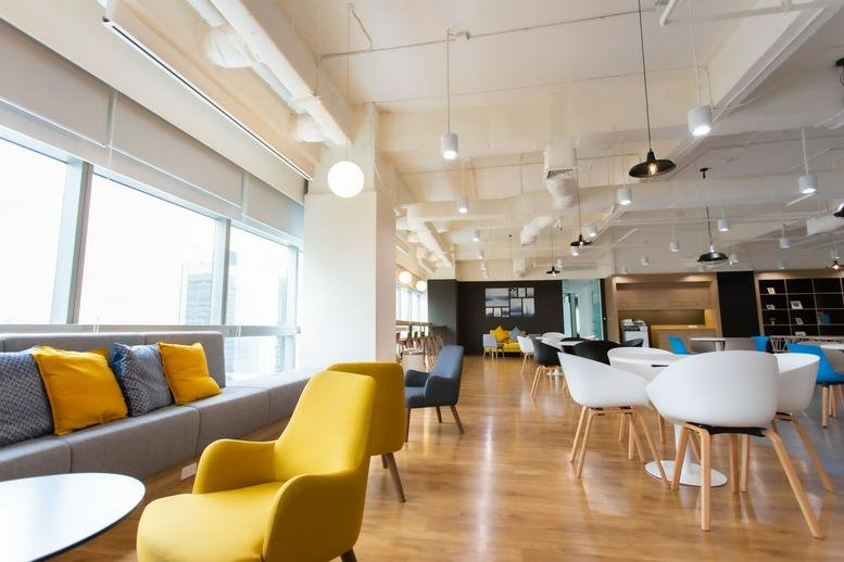 Vibrant office lounge with yellow armchairs, a grey sofa, and city views through large windows.