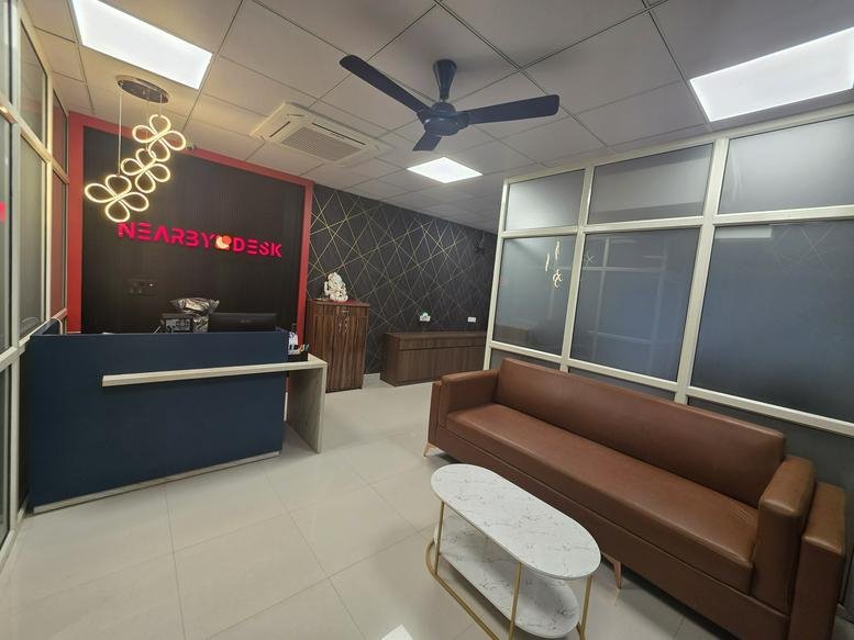 Branded reception area of Nearby Desk, 161-A/9 Mehrauli Road, featuring a blue front desk and a tan leather sofa.