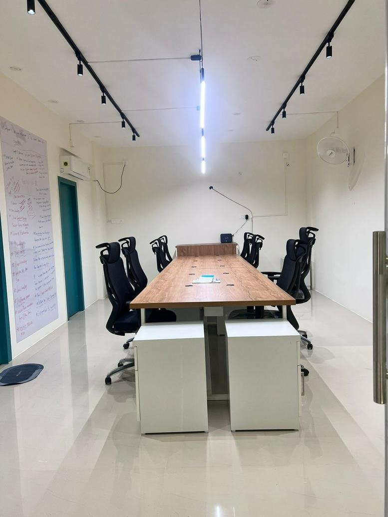 Spacious boardroom with a long wooden table, ergonomic black chairs, and track lighting.