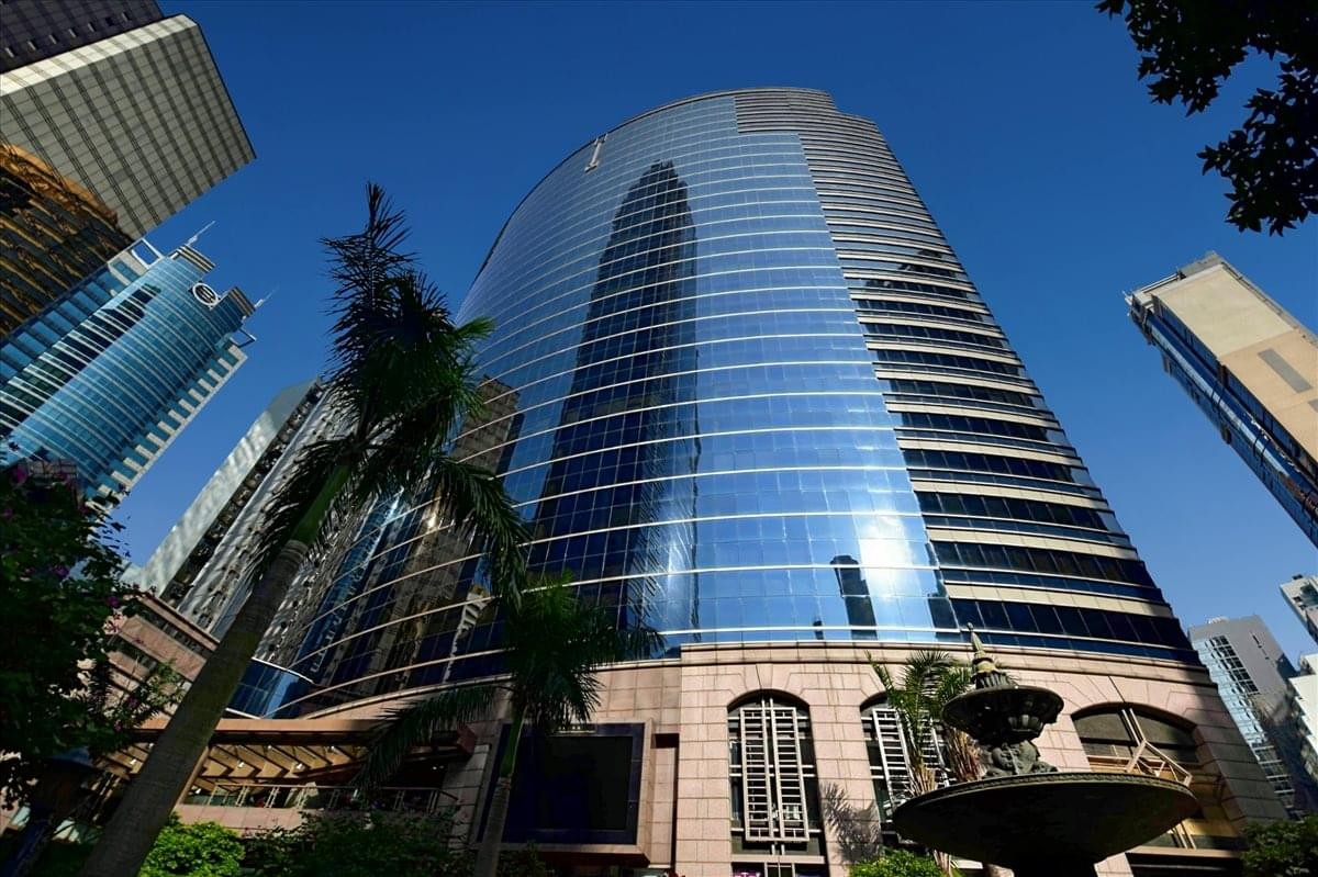 The sleek, blue glass exterior of the Grand Millennium Plaza skyscraper surrounded by other city buildings.