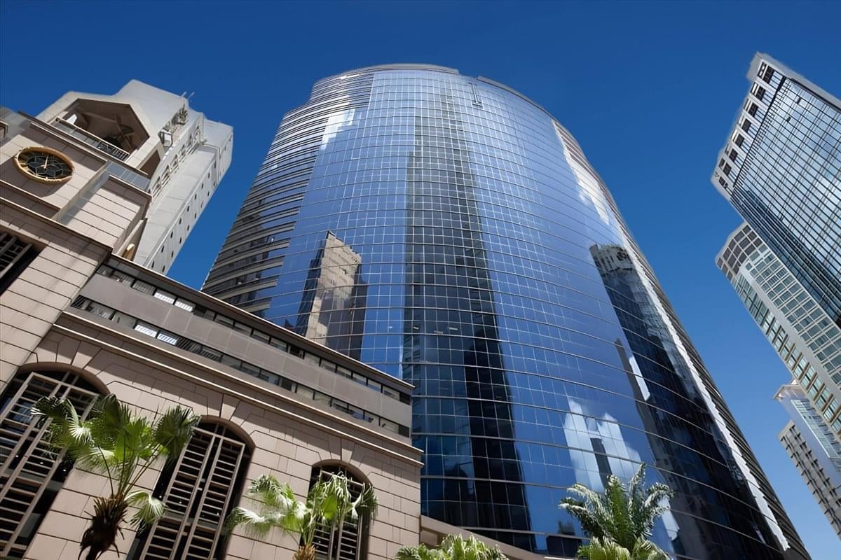 Sleek low-angle view of the curved glass office tower and surrounding city buildings.