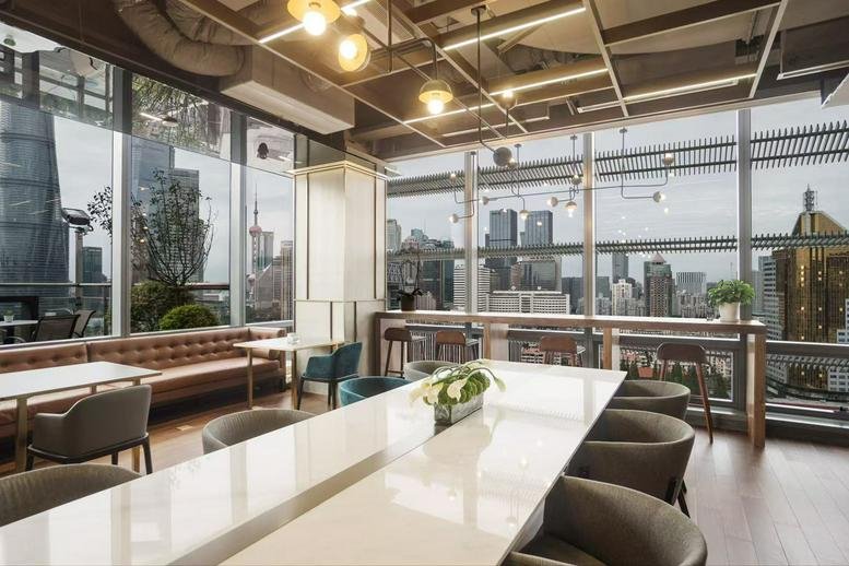 Bright coworking area with a long white table and city views through large windows.