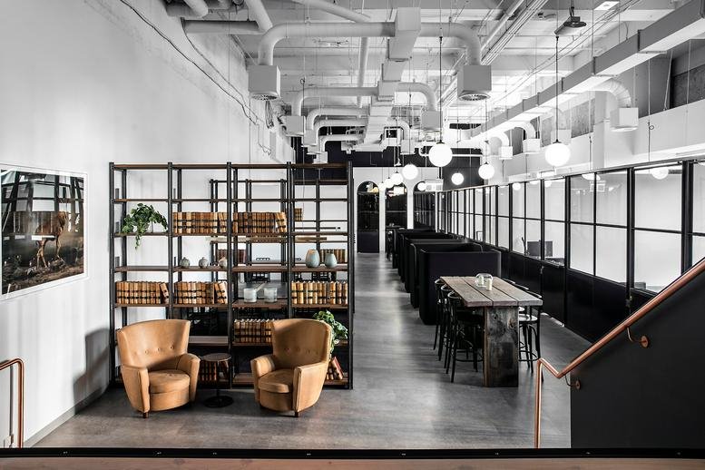Spacious common area at 201 Kent Street, Barangaroo with industrial ceilings, lounge chairs, and a large bookshelf.
