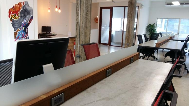Long white shared workspace desks at 205/19-21 Thonglor Road with vibrant wall art.