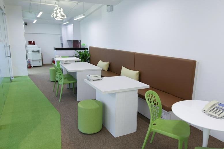 Spacious coworking area at The Mezzo with green stools, white tables, and long brown bench seating.