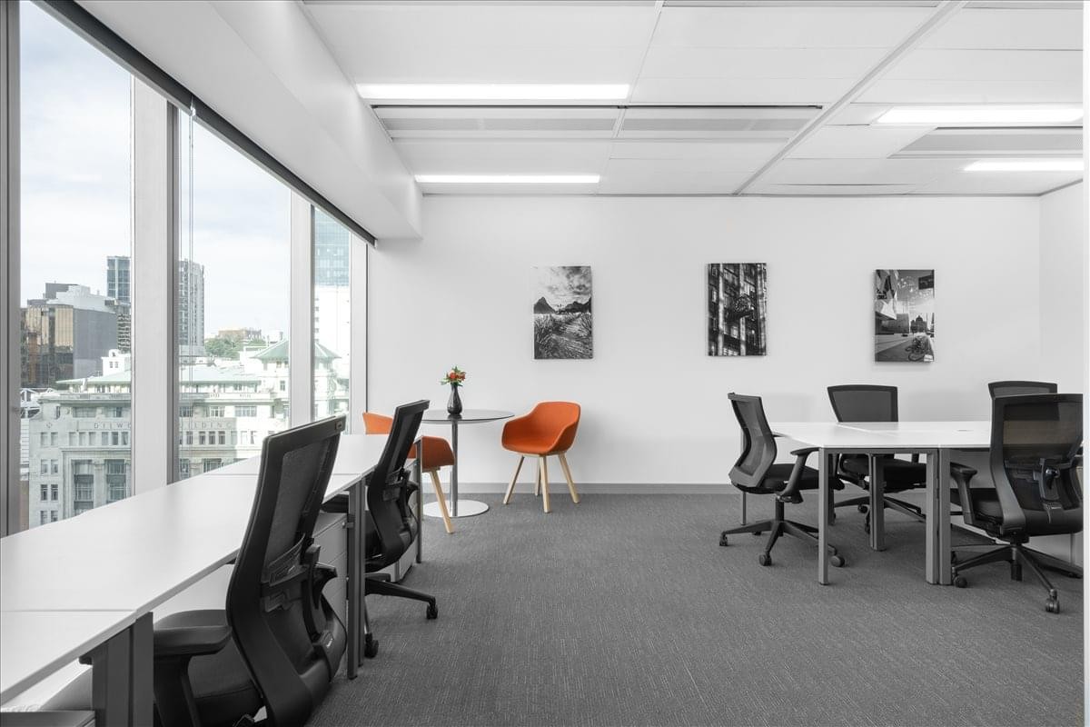 Luminous open-plan workspace at 21 Queen Street with desks, orange accent chairs, and city views.